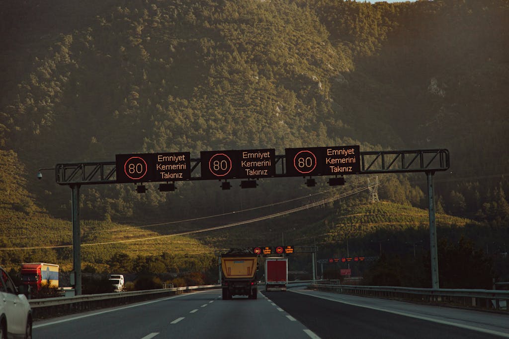Highway with speed limit signs against a mountainous backdrop and low traffic.
